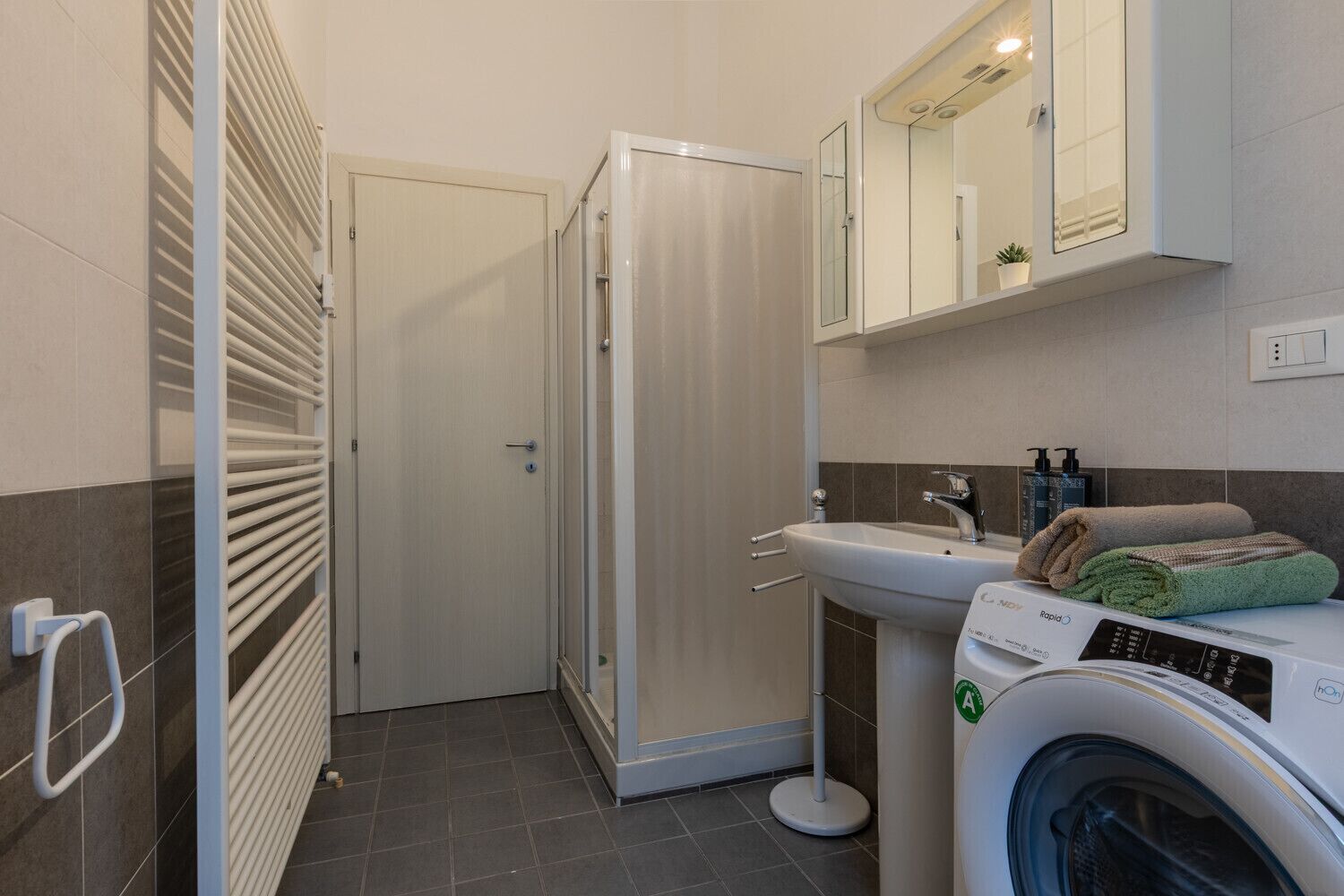 A bathroom with a shower, a sink, a mirror, and a washing machine.