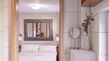 A hotel room with a bed, a large mirror, a bedside table with a lamp, and a wall-mounted radiator.