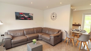 A living room with a sectional sofa, a coffee table, a dining area with a table and chairs, a wall clock, and a sports car painting. - 11 The Forge (Brampton)