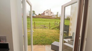 An open door leading to a backyard with a grassy area, a wooden fence, and a house in the background. - 11 The Forge (Brampton)
