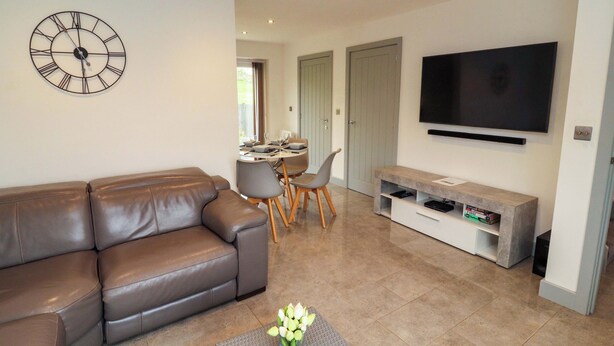 A living room with a brown leather sofa, a dining area with a table and chairs, a wall-mounted clock, and a flat-screen TV. - 11 The Forge (Brampton)