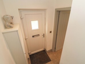 Uma porta branca com uma pequena janela, um tapete de entrada e um relógio fixado na parede.