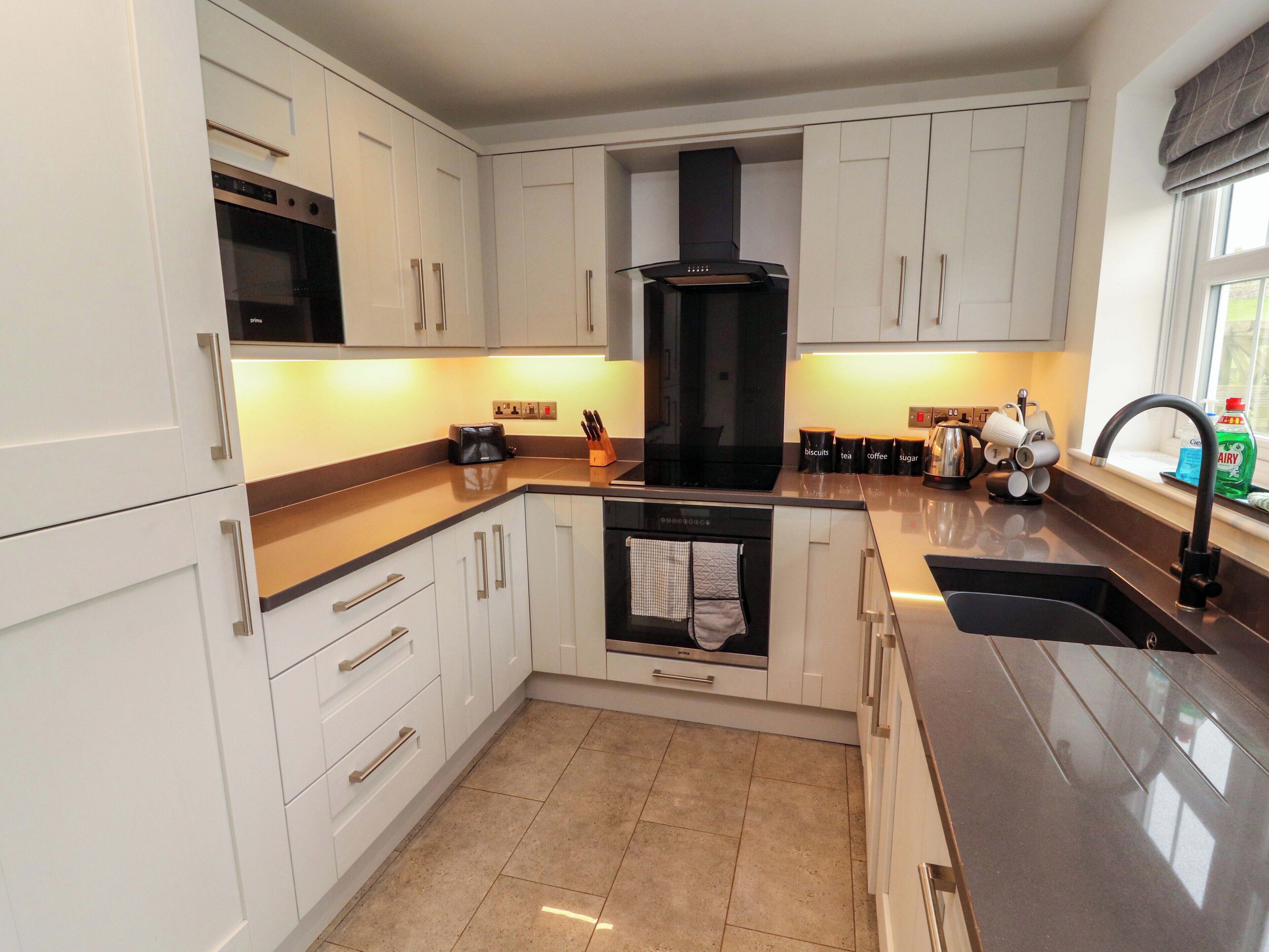 A modern kitchen with white cabinets, a built-in oven, a black range hood, and a stainless steel sink.