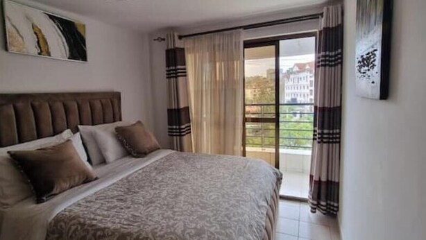 A bedroom with a large bed, a headboard, and a view of a building through the window. - Cozy 1-Bedroom Apartment in Westpark Heights (flyover)