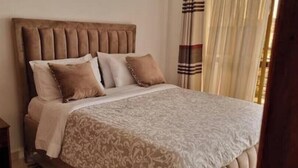 A bedroom with a tufted headboard, a patterned bedspread, and a bedside table with a lamp. - Cozy 1-Bedroom Apartment in Westpark Heights (flyover)