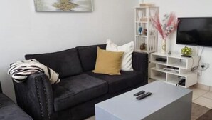 A living room with a black sofa, a white coffee table, a TV on the wall, and a white shelving unit. - Cozy 1-Bedroom Apartment in Westpark Heights (flyover)