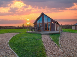 A log cabin with a large glass front, a porch with chairs, and a gravel path leading to it. - Lodge 3, Thorpe-On-The-Hill (Lincoln)
