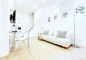 Ein modernes Wohnzimmer mit einem weißen Sofa, einem Essbereich mit Stühlen und Kunstwerken an den Wänden.