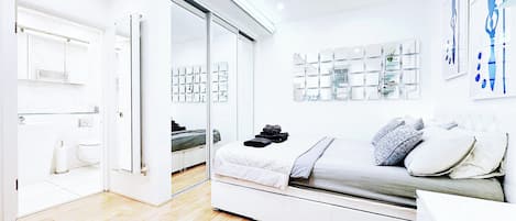 A modern bedroom with a bed, bedside tables, a wardrobe, and a bathroom visible through a glass door.