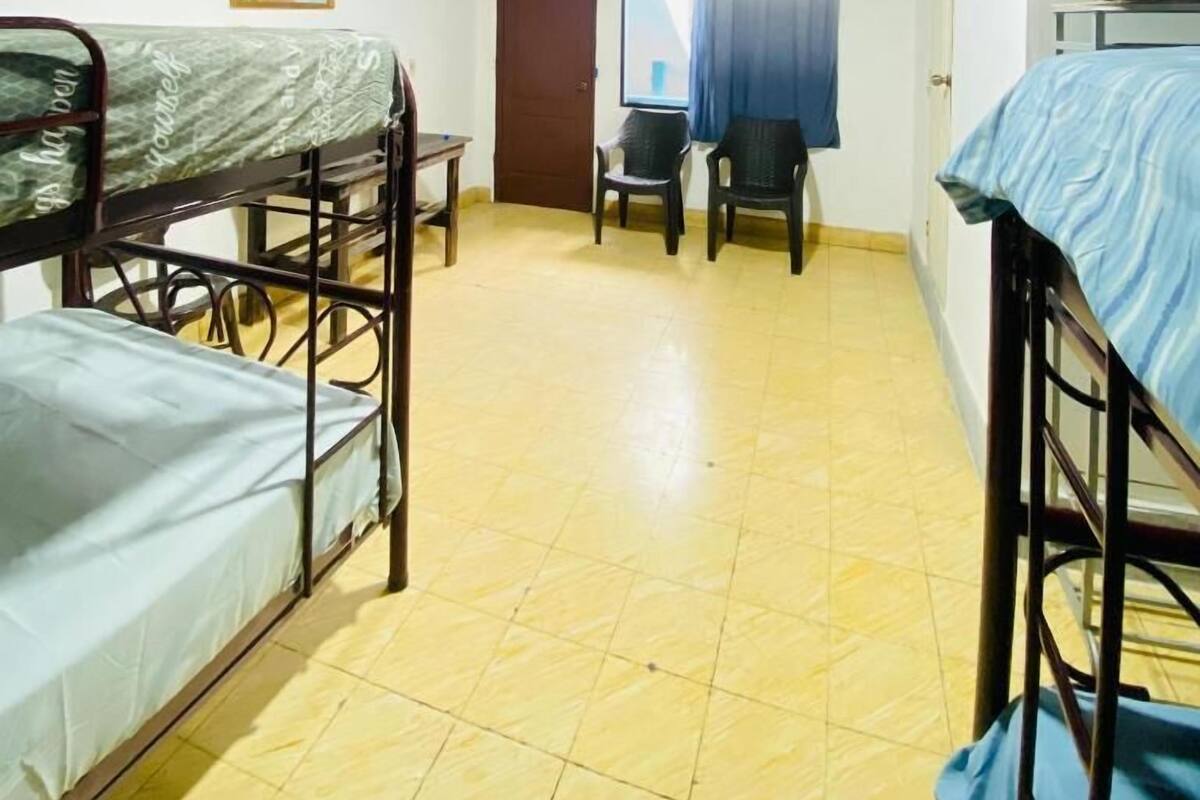 Una habitación con literas, una mesita, una silla y una puerta que da a otra habitación.