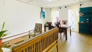 Una habitación con un banco de madera, una mesa, sillas, un televisor y una ventana con cortinas.