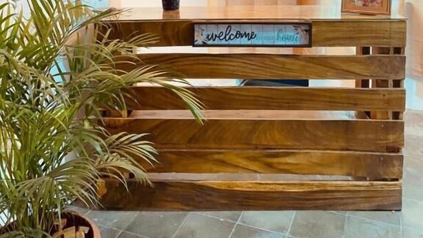Un banco de madera con un letrero que dice 'welcome', un florero con flores rojas y una planta.