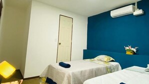 Habitación de hotel con dos camas, un escritorio con lámpara, una puerta y un equipo de aire acondicionado en la pared.