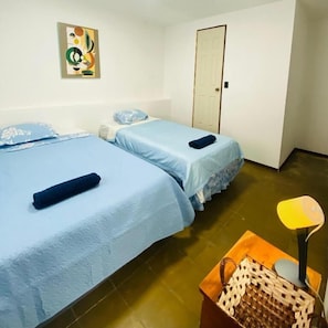 A room with two beds, a door, a wall art piece, and a lamp. - Hostal la.casa de Ross (Santa Ana)