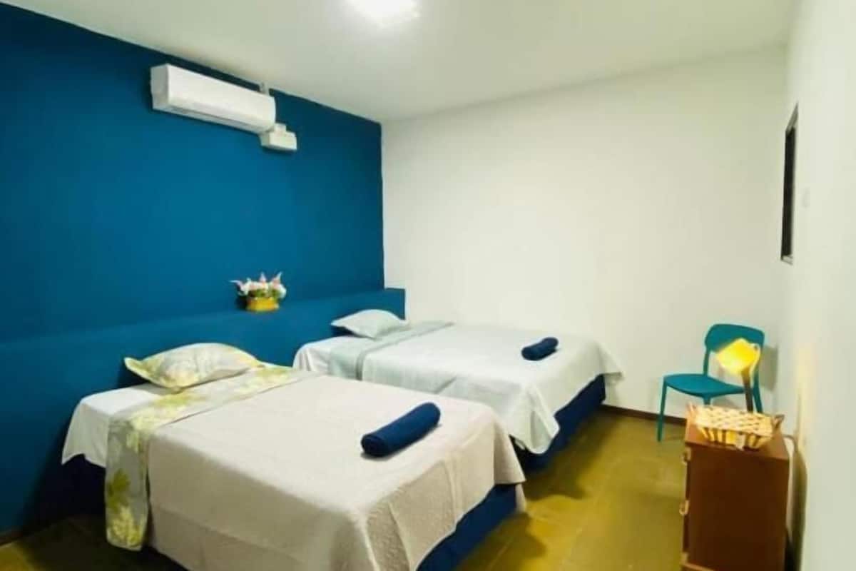 Una habitación con dos camas, una pared azul decorativa, un ventilador de techo y una pequeña mesa con una silla.
