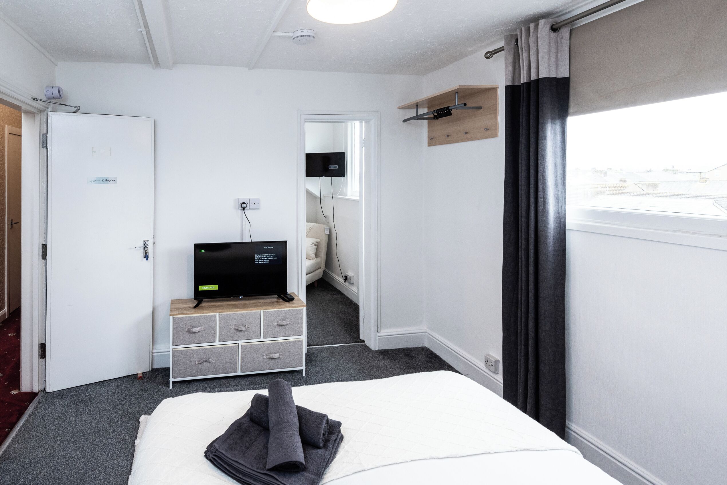 Une chambre d’hôtel avec un lit, une télévision, une commode, un miroir et une fenêtre avec des rideaux.