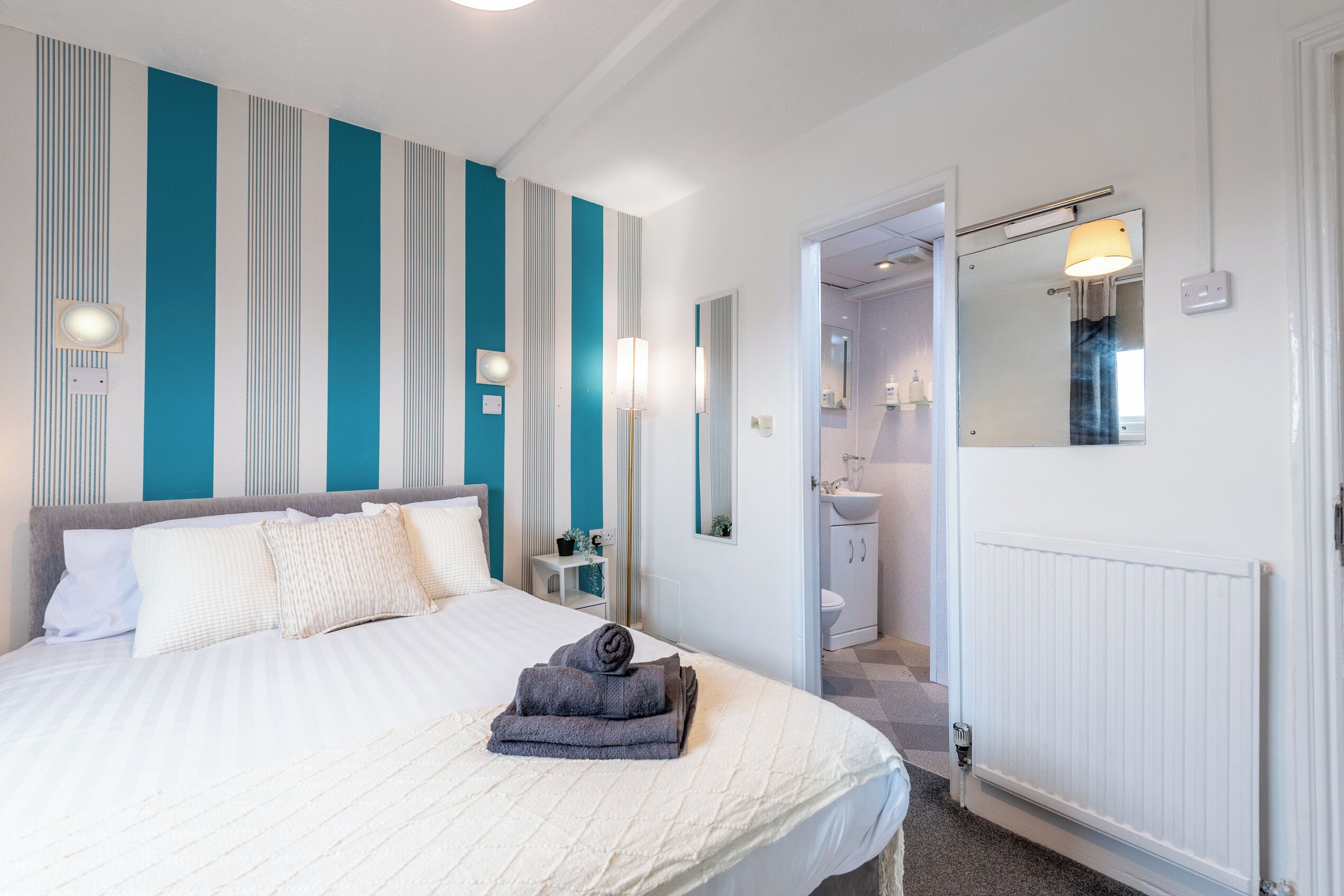 Hotellihuone, jossa on sänky, kylpyhuone peilillä ja patteri.