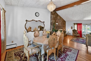 Une salle à manger avec une table ronde, des chaises décorées, un lustre et un mur en pierre.
