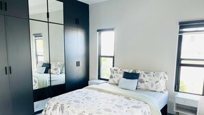 Un dormitorio con cama, armario, mesita de noche y ventana.