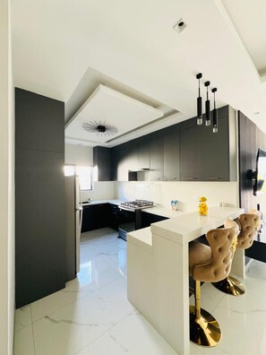 A modern kitchen with dark cabinetry, a white countertop, and a central island with bar stools. - Beautiful 2-bedroom house with AC in charming St. Ann Parish (St. Ann Parish)