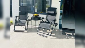 Un patio con dos sillas negras y una mesa pequeña, una ventana grande y una puerta.