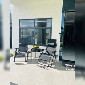 A patio with two black chairs and a small table, a large window, and a door. - Beautiful 2-bedroom house with AC in charming St. Ann Parish (St. Ann Parish)