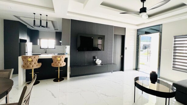 Una sala de estar moderna con piso de mármol, una mesa de centro de vidrio, un sofá y una zona de cocina con televisor y chimenea.