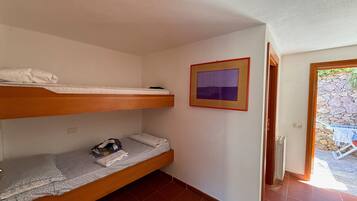 A room with two bunk beds, a framed picture on the wall, and a door leading to an outdoor area with a stone wall.