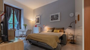 Una camera da letto compatta con un letto, un comodino, una lampada e una scrivania con una sedia.
