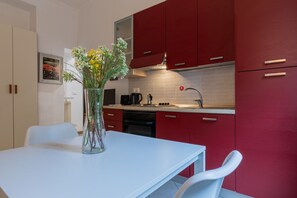 Een moderne keuken met rode kastjes, een wit aanrecht en een vaas met bloemen op de tafel.