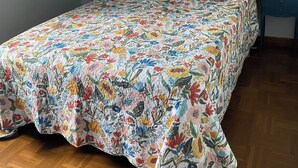 A bedroom with a floral bedspread, a painting above the bed, and two bedside tables with lamps.