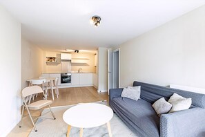 A modern living room with a sofa, a small round table, and a kitchen in the background. - Belgravia Living Modern 2-bed Flat Near Victoria (London)