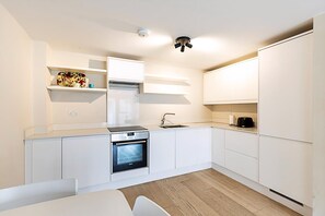 A modern kitchen with white cabinetry, a built-in oven, a sink, and a coffee maker. - Belgravia Living Modern 2-bed Flat Near Victoria (London)