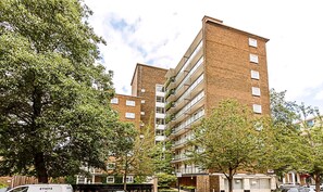 A multi-story building with a brick facade, large windows, and balconies with greenery. - Belgravia Living Modern 2-bed Flat Near Victoria (London)