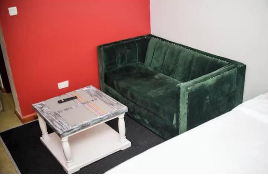 A room with a green velvet sofa, a white table, and a red wall.