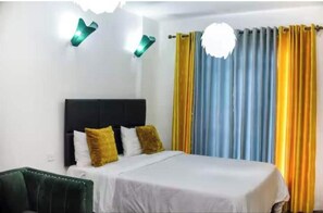 Ein Hotelzimmer mit einem Bett, einem Kopfteil, einem grünen Sessel und Vorhängen.