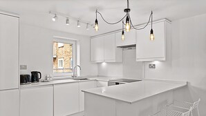 A modern kitchen with white cabinetry, a large island, pendant lighting, and a view of a brick building outside. - Belgravia Living 2-bed, 2-bath Fourth Floor Apartment (London)