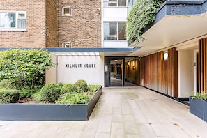 A modern building entrance with a sign reading 'KILMUIR HOUSE,' a paved pathway, and a well-maintained garden area. - Belgravia Living 2-bed, 2-bath Fourth Floor Apartment (London)