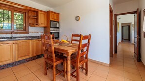 A kitchen with wooden cabinets, a dining table with chairs, a microwave, and a clock on the wall. - Nice Villa in Sant Carles With Pool (Santa Eulalia del Rio)
