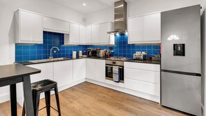 A modern kitchen with white cabinets, a stainless steel range hood, a built-in oven, and a refrigerator. - Charming Golborne Escape (London)