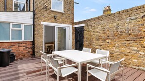 A patio with a white table and chairs, a brick wall, and a door leading to a room. - Charming Golborne Escape (London)