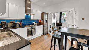 A modern kitchen with white cabinets, a blue backsplash, stainless steel appliances, and a dining area with a black table and stools. - Charming Golborne Escape (London)