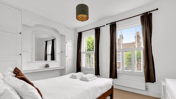 A bedroom with a bed, a mirror, a window with curtains, and a radiator. - Charming Golborne Escape (London)