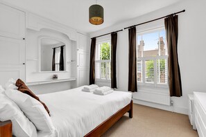 Quarto com cama, espelho, janela com cortinas e radiador.