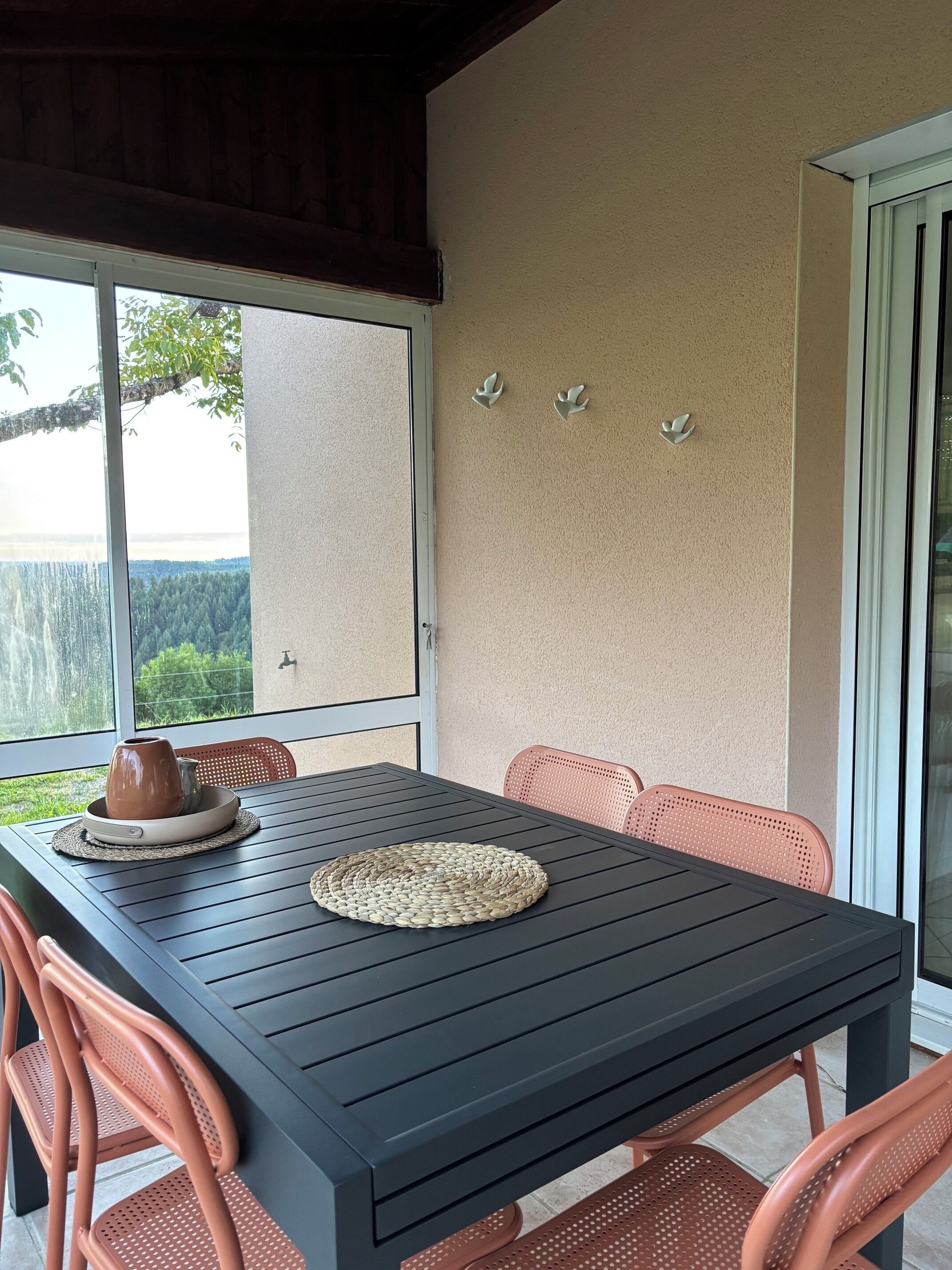 Uma área de pátio com mesa, cadeiras, um muro decorativo e vista para o verde.