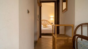 Un pasillo que conduce a un dormitorio con una cama, una lámpara de noche y una silla.