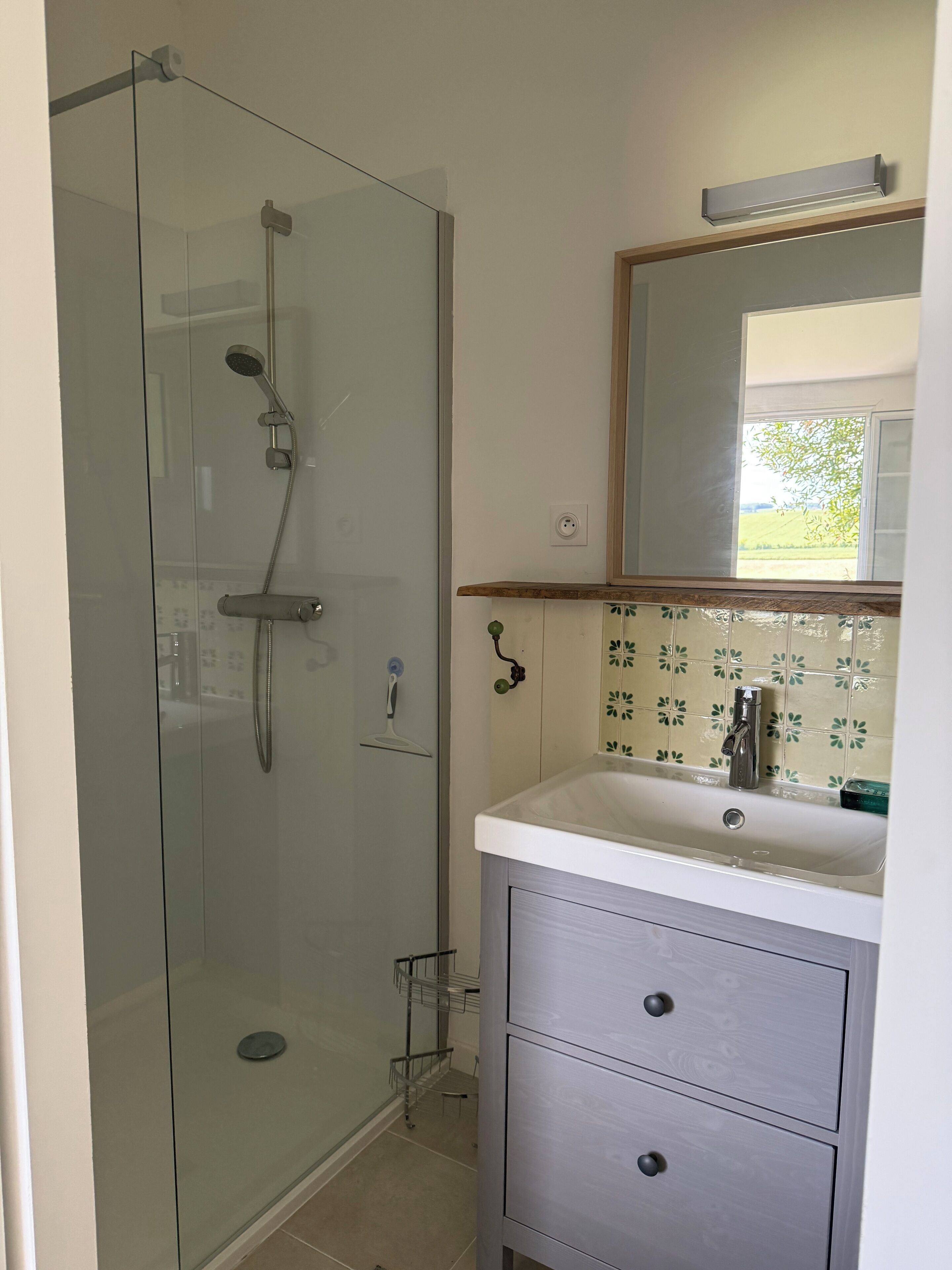 A bathroom with a glass-enclosed shower, a sink with a mirror above, and a tiled backsplash.