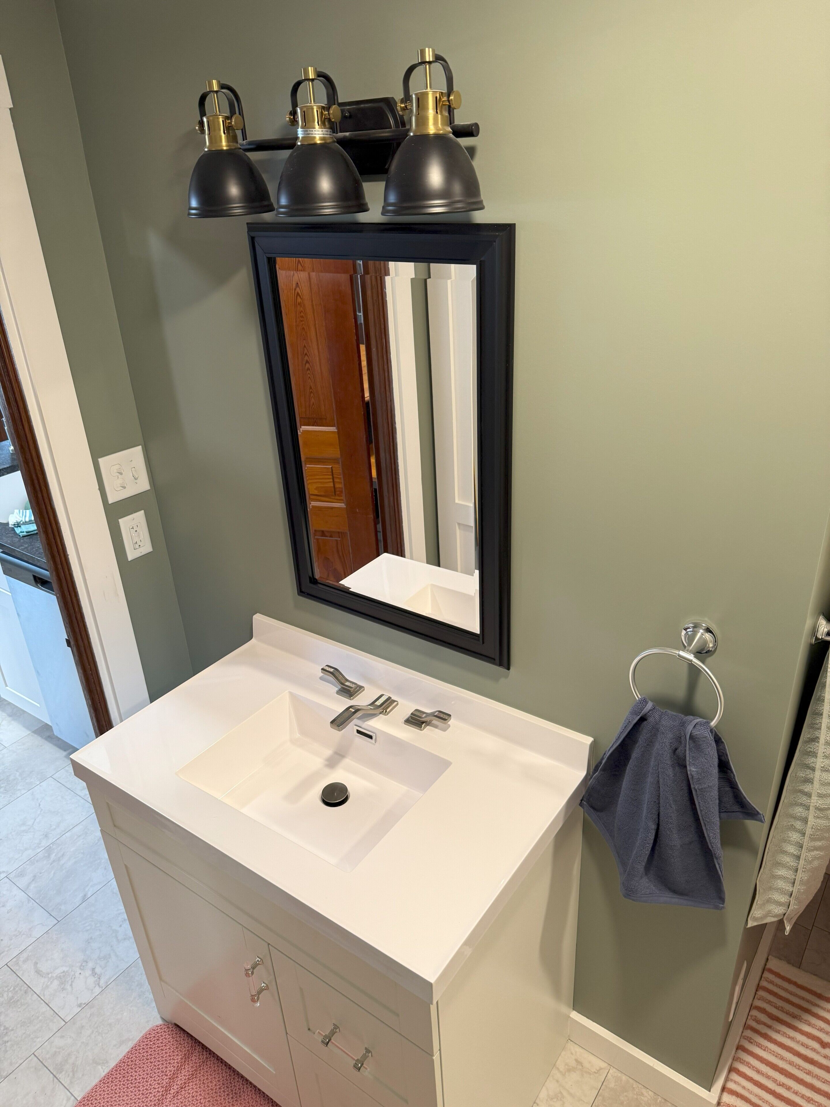 Une salle de bain avec un lavabo blanc, un miroir et trois lampes noires fixées au mur.