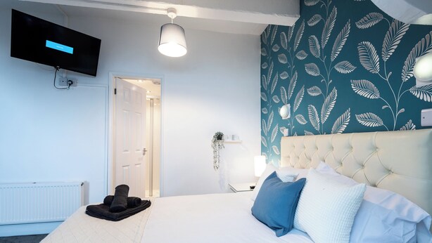 Une chambre à coucher avec un lit, un téléviseur fixé au mur, une porte et un mur décoré d’un motif.