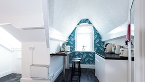 Une cuisine compacte avec une fenêtre, un petit tabouret et un plan de travail équipé d’appareils électroménagers.